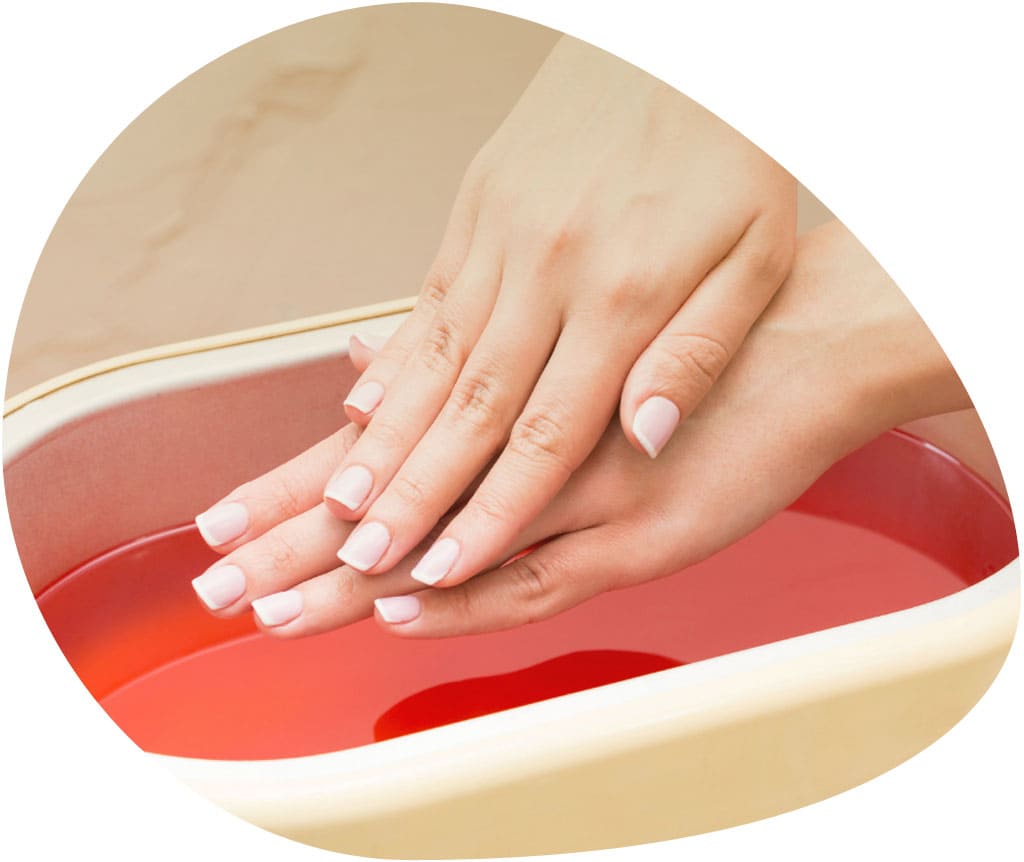Manicura y baño de parafina para calmar el dolor y relajar los músculos. Unas manos están entrando en el baño de parafina color rojo